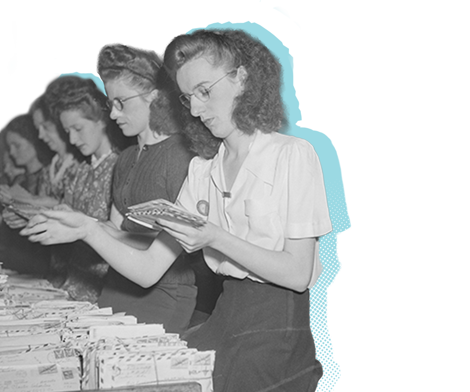 A row of postal employees sort mail from a table filled with letters.