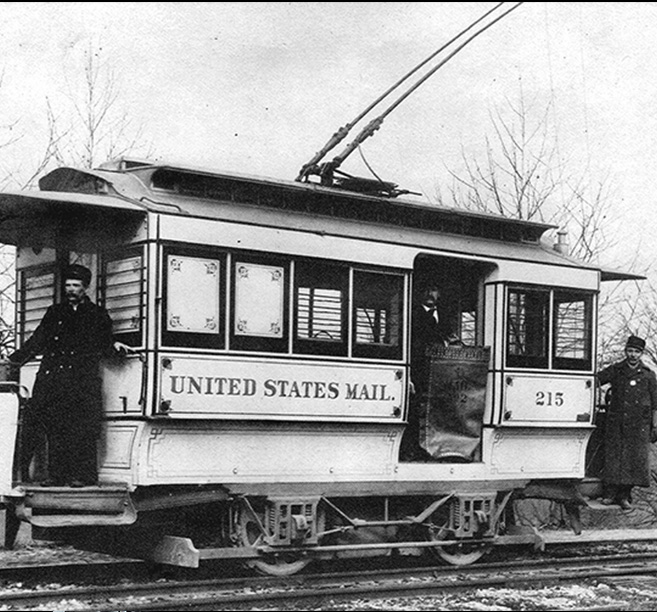 A black-and-white photograph of three men standing in a mail trolley.